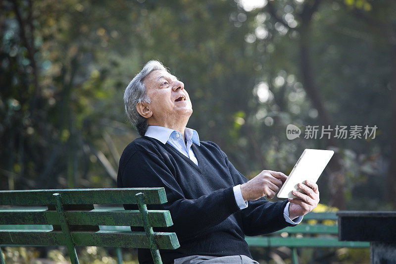 一名男子在公园边玩平板电脑边笑