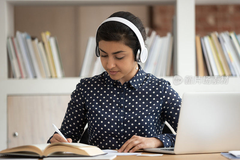 专注于准备考试的印度女学生，戴着耳机。