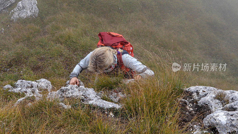 女登山家爬上长满草的悬崖