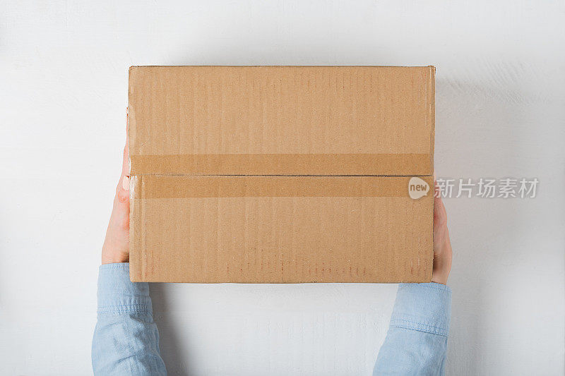 女性手中的大方形纸箱。俯视图，白色背景