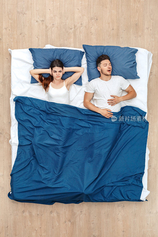 睡觉前。年轻男子睡觉打呵欠，而女人捂着耳朵关心毯子在床上俯视图