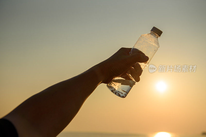 在夕阳下，男人手里拿着水晶般清澈的水瓶