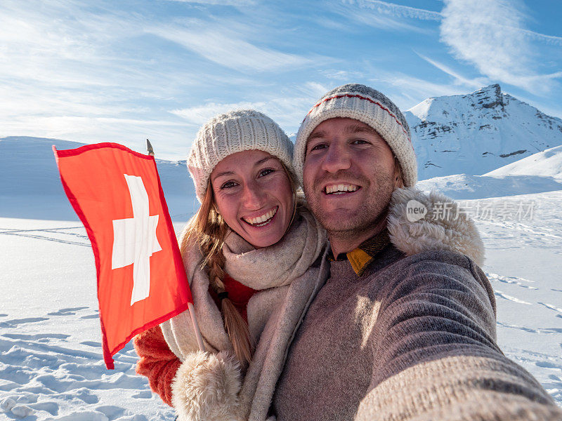 一对夫妇在瑞士阿尔卑斯山白雪皑皑的山上与瑞士国旗自拍