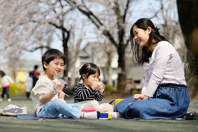 母亲和两个孩子在樱桃树下吃午饭
