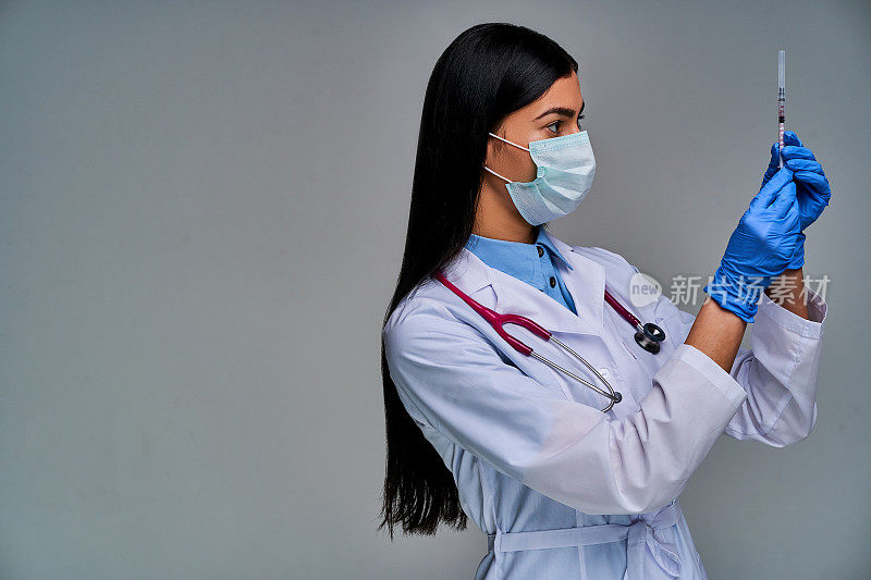 女医生戴着面罩，肩上戴着语音内窥镜，戴着蓝色医用手套，手里拿着注射器。医学的概念
