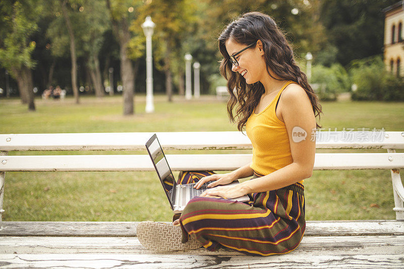 坐在公园长椅上用笔记本电脑的女人