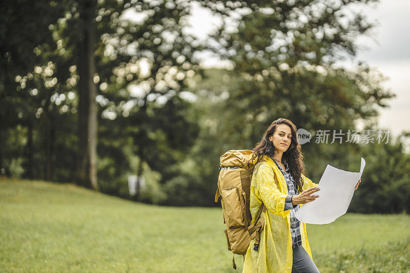 年轻女子穿着防水夹克，看地图，在雨中徒步旅行