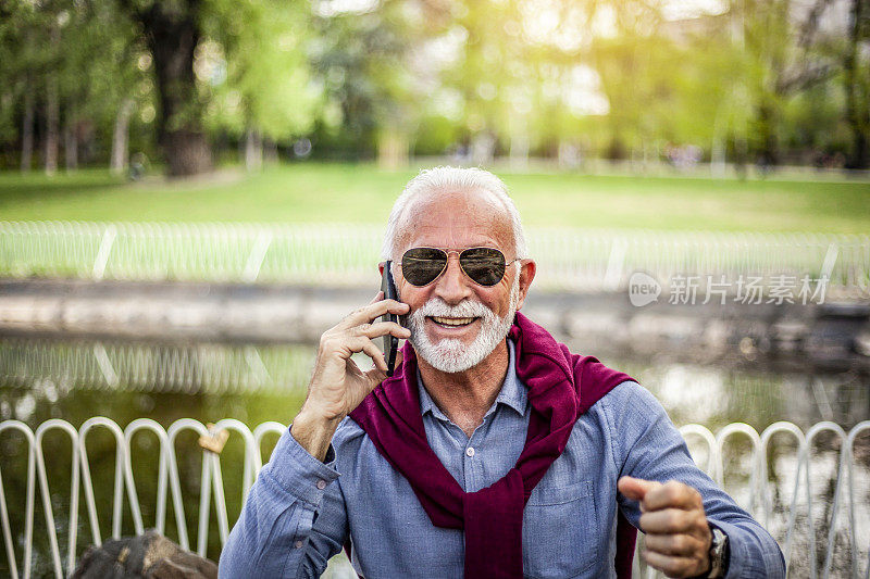 老人愉快地讲电话，笑出声来——一个老人正在户外讲手机