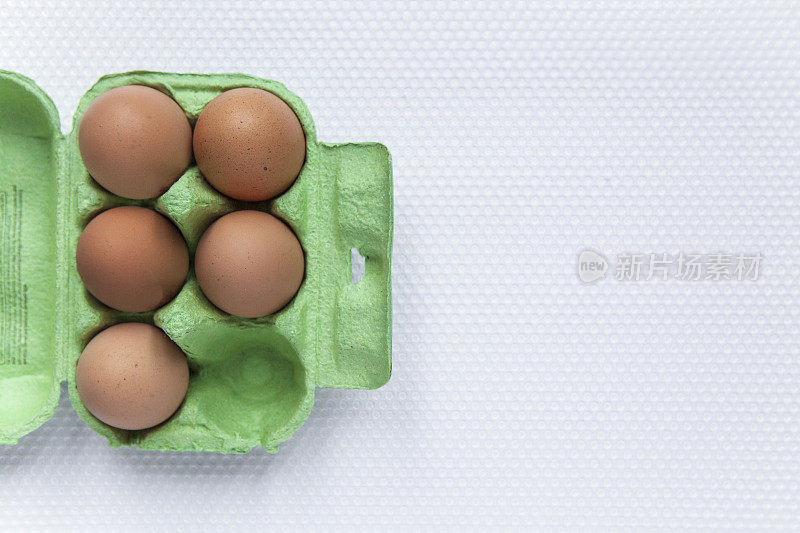 5个鸡蛋放在一个绿色的硬纸板鸡蛋盒上，在一个塑料窝纹表面上直接用拷贝空间观看