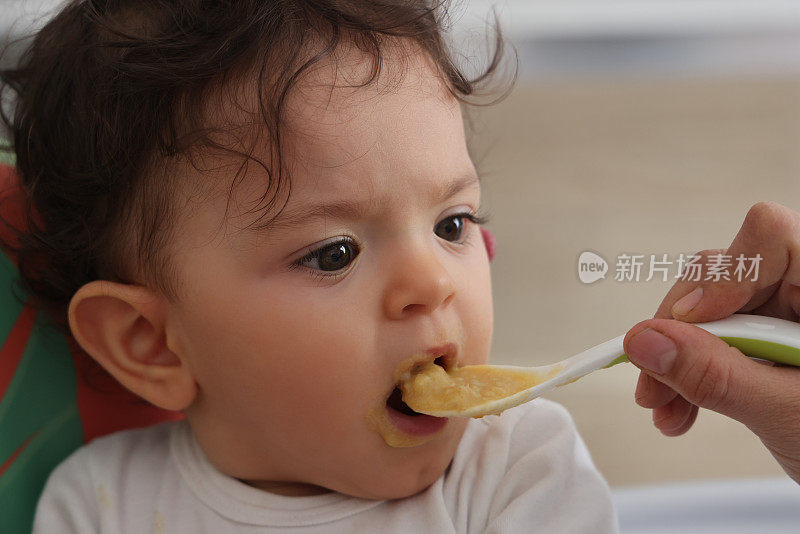 妈妈用厨房里的勺子喂婴儿。