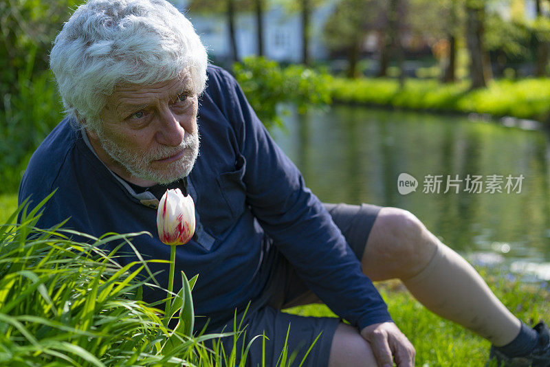 一位老年PD患者坐在郁金香附近的草地上，一边欣赏着斯洛文尼亚Kočevje河的景色。