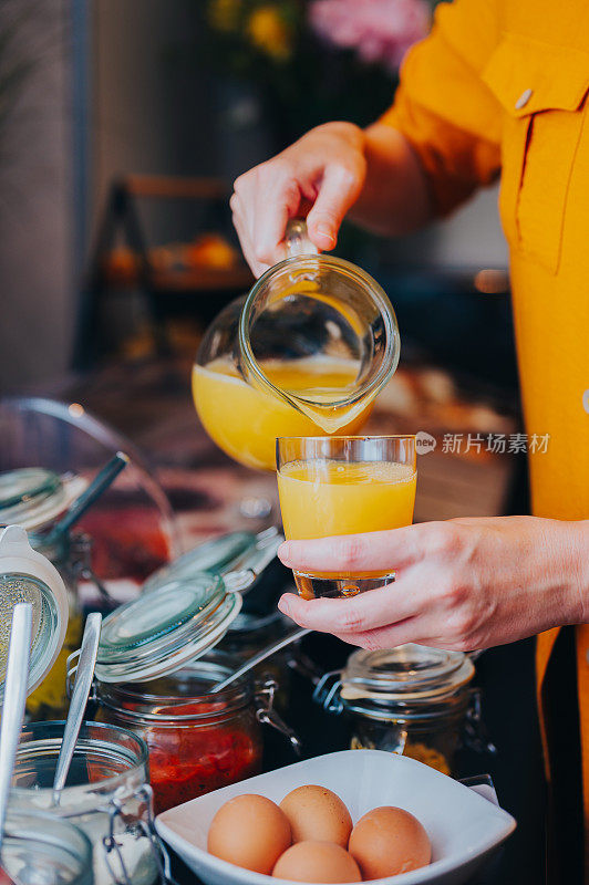在饭店餐厅的自助餐台上，把橙汁倒进玻璃杯里