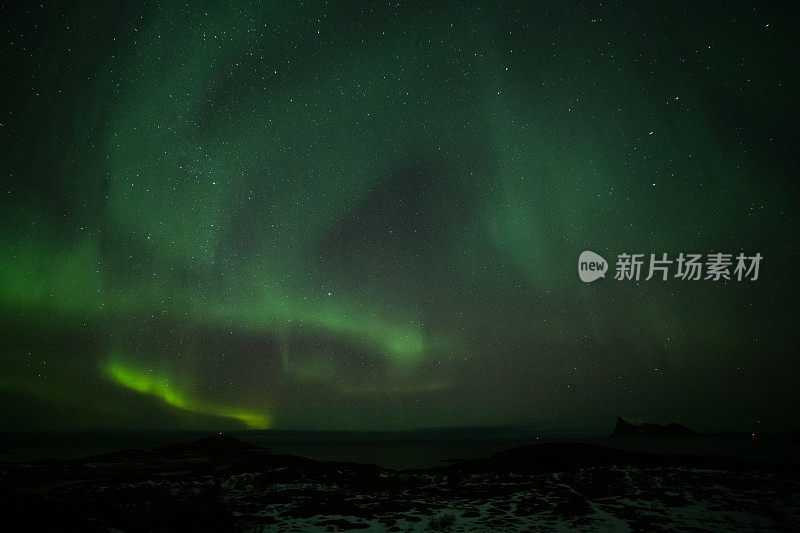 北极光在夜空中山脉的轮廓。长曝光，多色灯光