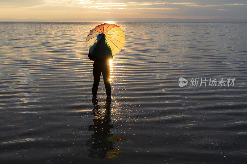 女人撑着雨伞在盐湖风景中看日落