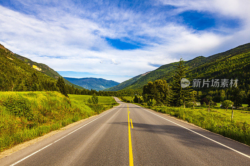 公路旅行场景与阳光和开阔的道路与蓝天，丰富的绿色山脉和山谷