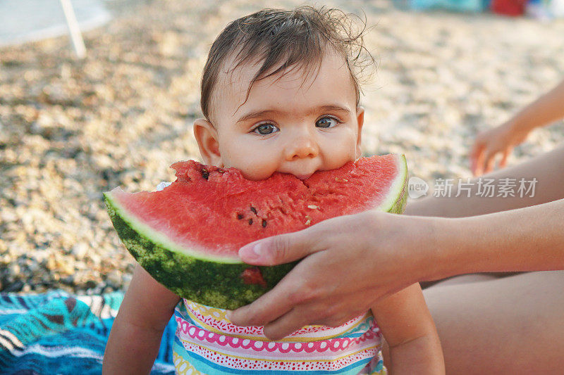 妈妈在海滩上用西瓜喂她的小女儿