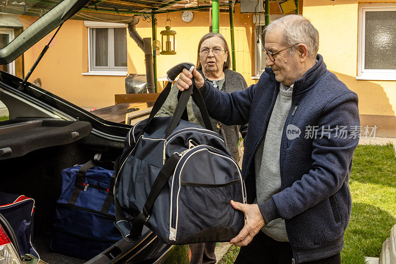 一对老夫妇把旅行袋放在汽车的后备箱里，因为他们要去度假。