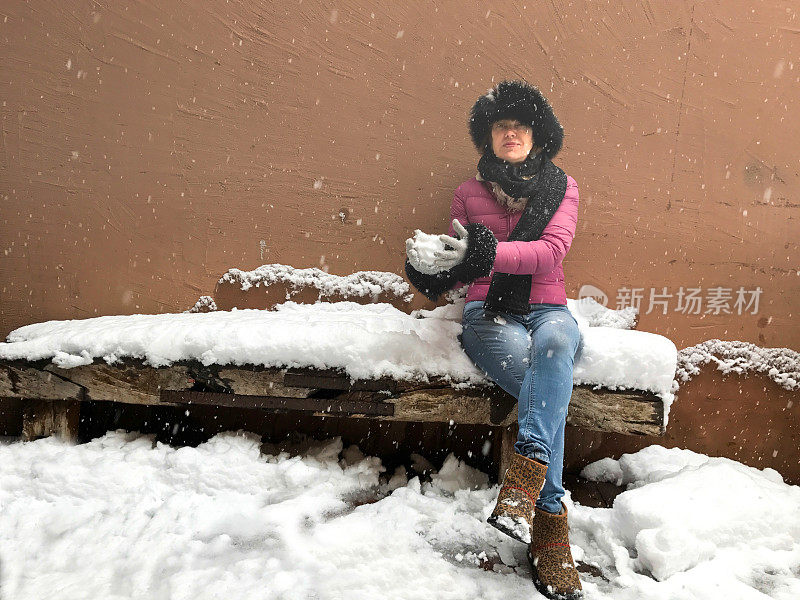 下雪:女人坐在下雪的长凳上堆雪球