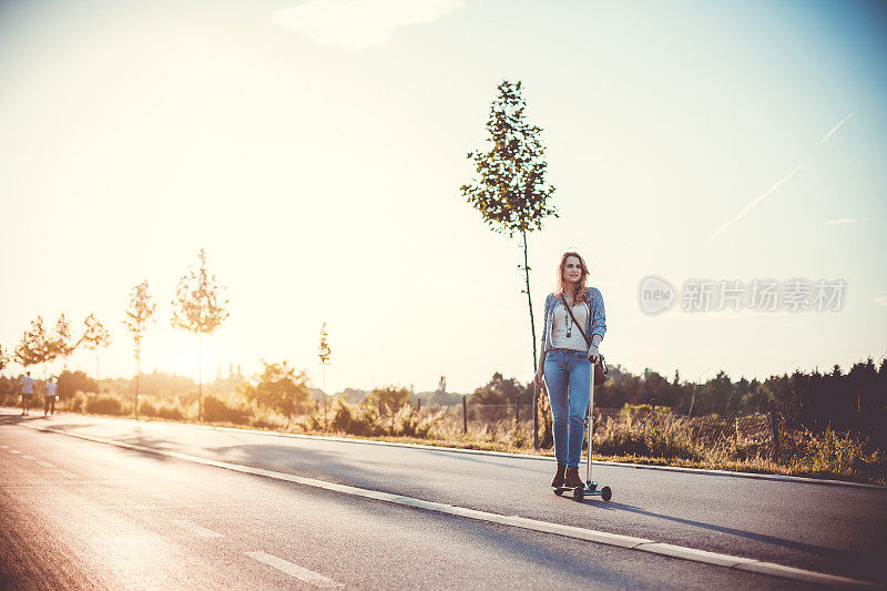 微笑的女人骑着推滑板车在自行车道上