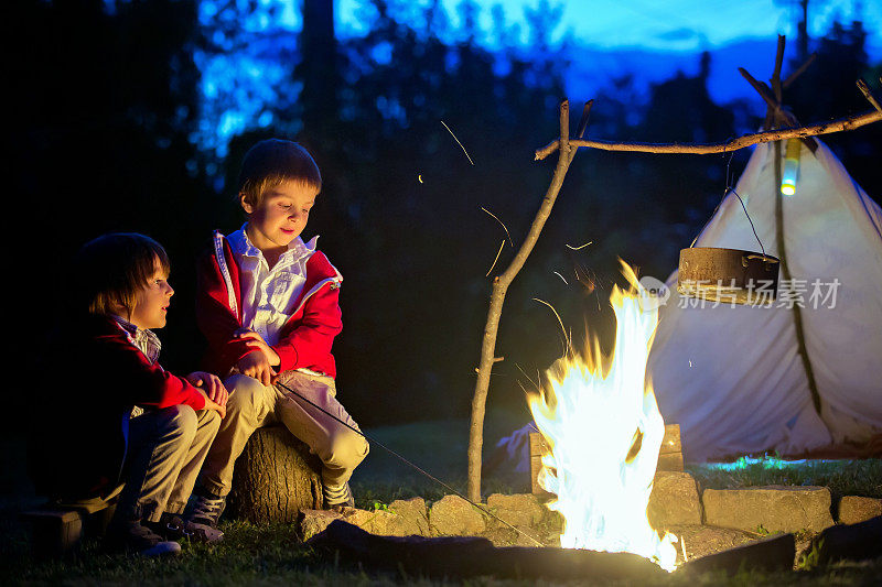 两个可爱的男孩，在日落后围坐在篝火旁，听着恐怖的故事
