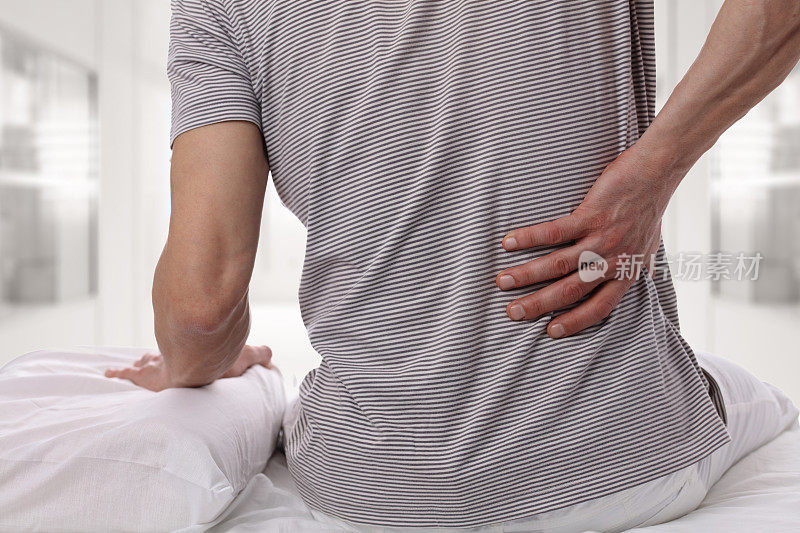 男人在卧室里忍受着背部疼痛。不舒服的床垫和枕头会导致背痛。