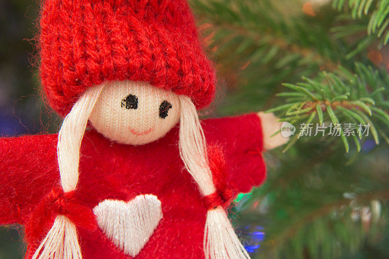 圣诞树上戴着红色无檐帽的羊毛手工娃娃(特写)