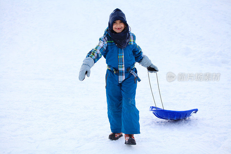 快乐的女孩穿着雪衣和塑料雪橇