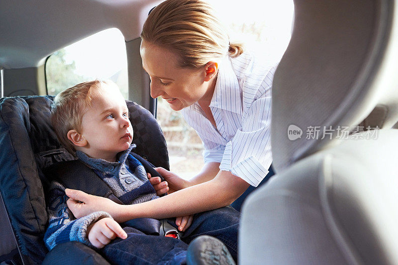 一个照顾孩子的女人在汽车座椅上保护着她的小儿子