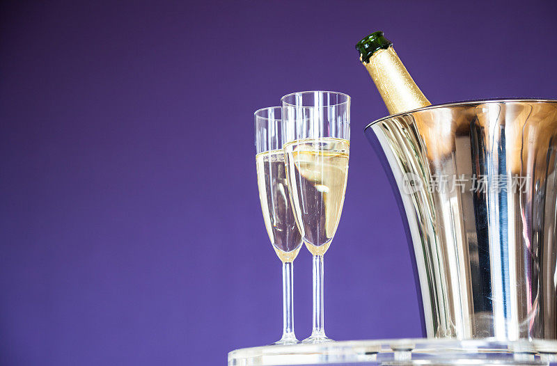 在紫色的背景下，装满香槟的酒杯和酒瓶