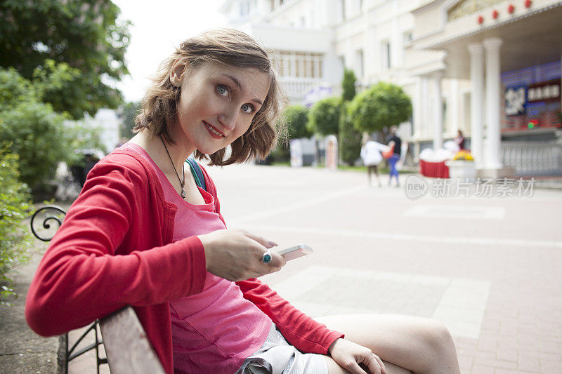 坐在长椅上拿着智能手机的女孩