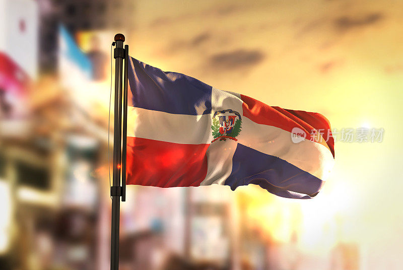 在日出的背光下，城市模糊的背景下的多米尼加共和国国旗