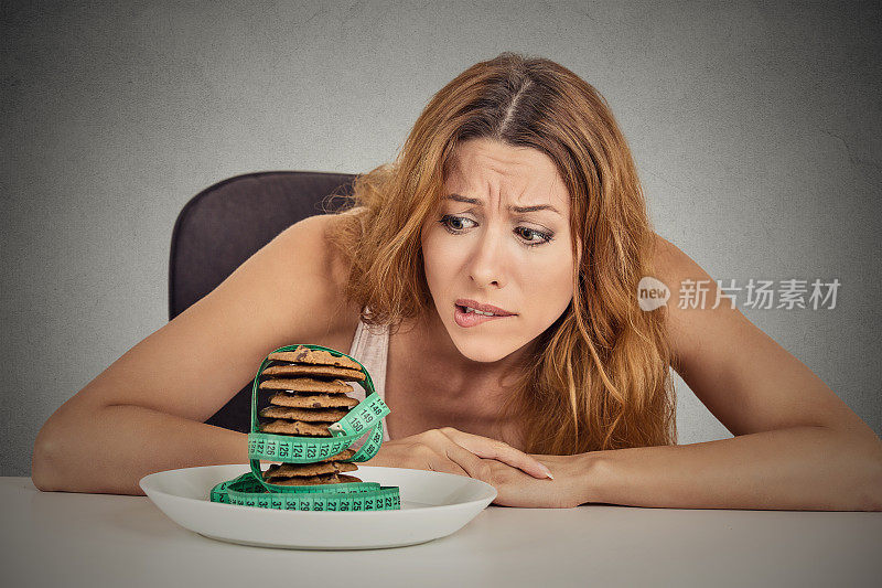 描绘一个年轻的不快乐的女人，她渴望着甜甜饼干，但又担心坐在餐桌前体重会增加