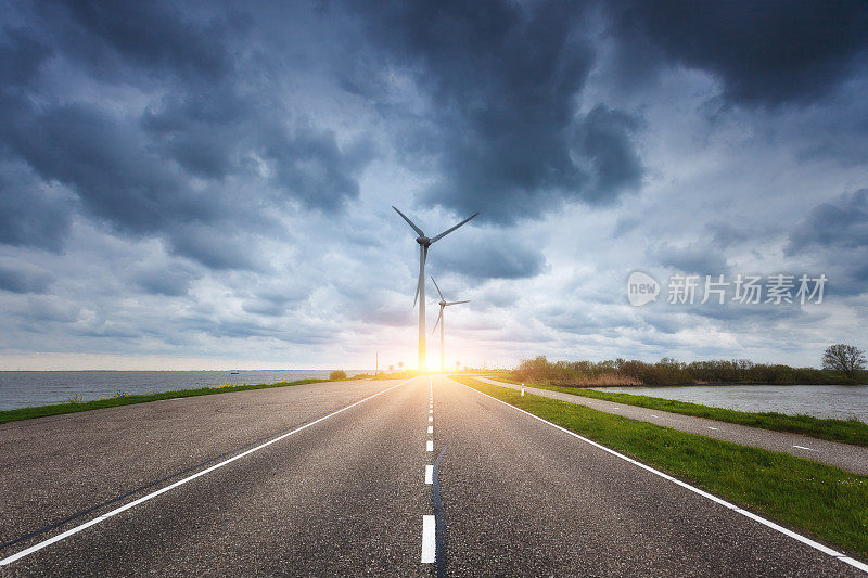 美丽的柏油路和风力发电机在日落发电。用于发电的风车。春天的风景有公路、绿草、风车和蓝天