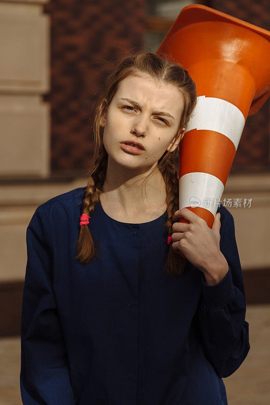 年轻漂亮可爱的女孩拿着橙色的路障标志锥形塑料