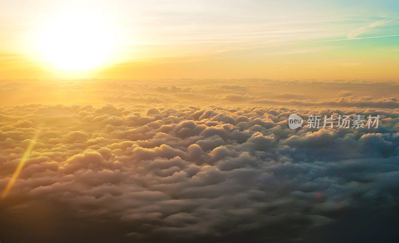 在温暖的黄色灯光下，日出时许多白色蓬松的云，如梦似幻。地平线上的蓝天。在晴朗无云的日子里乘飞机旅行。奇妙和壮丽的感觉