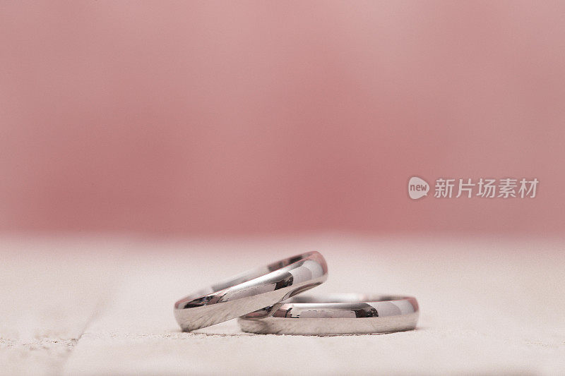 婚礼戒指在一个木制桌子上的宏观视图与粉红色的背景