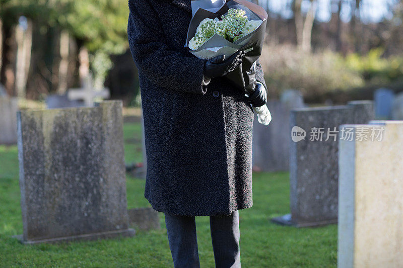 年长妇女与鲜花站在墓旁的特写