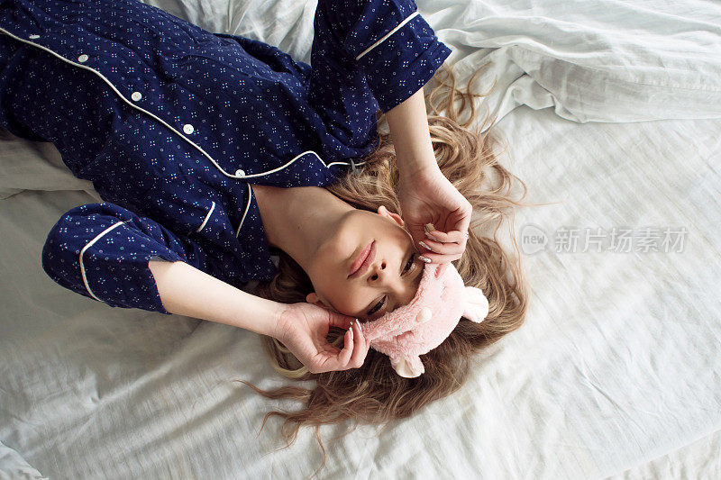 可爱的金发女郎穿着蓝色睡衣躺在床上，戴着睡眠面罩，俯视图