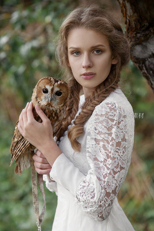 带着一只猫头鹰的美丽浪漫的女人。鸟落在她手上。