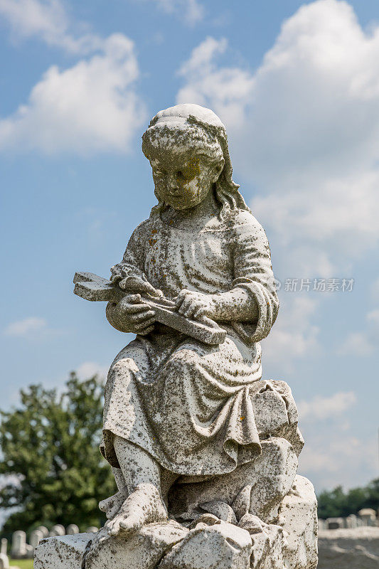 小女孩的雕像举着十字架和花在一个公共墓地