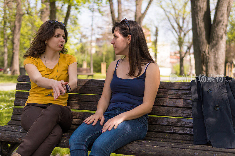 两个白人女孩坐在公园的长椅上聊天