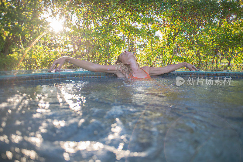 在度假村温泉的热水浴缸健康在热带天堂-女人放松在豪华度假村温泉撤退的室外热水浴缸池。快乐的年轻女模特放松休息在水上度假旅游。