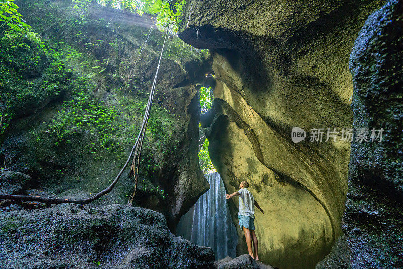 在巴厘岛的热带雨林中，一名旅行的年轻人张开双臂拥抱大自然的美丽。人们以自然为旅游理念。