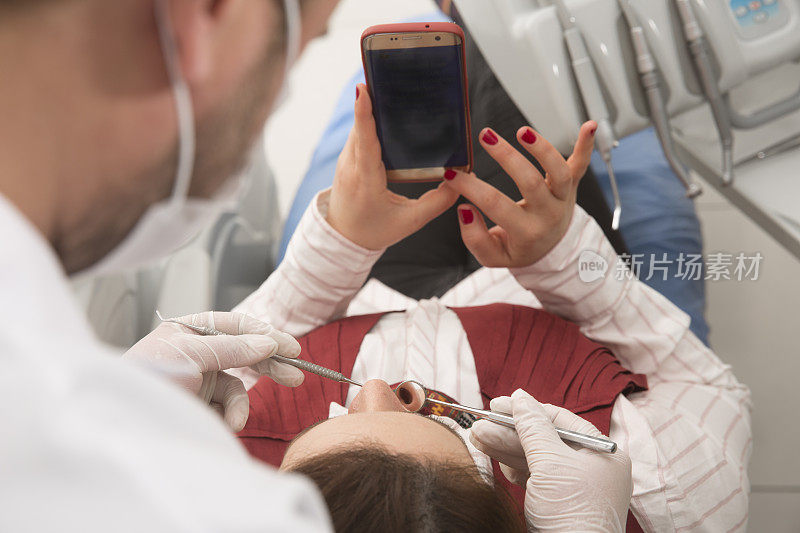 电话成瘾的女性病人照顾她的手机，同时进行牙医治疗