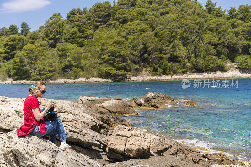 克罗地亚Mljet岛，一位坐在海边岩石上吃三明治的资深女士的侧视图