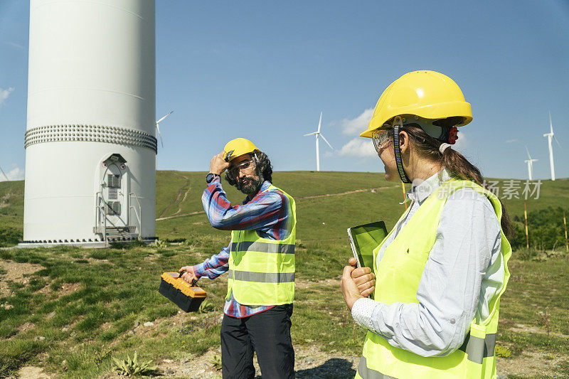 风力涡轮机农场的可再生能源系统工程。电力维护工程师在风力涡轮机发电站附近工作，身后是晴朗的蓝天。