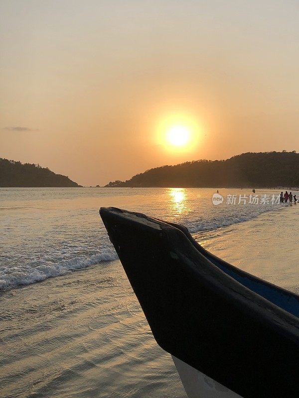 图像的日落在果阿海滩海在夏季日落，Palolem，南果阿，印度，度假，橙色的日落倒影照片与木制渔船剪影，拍打的海浪在热带海岸和海岸线上的棕榈树的背景