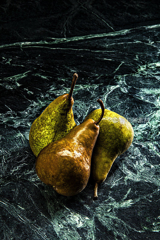 这是一张忧郁的照片，三个梨放在大理石绿色的背景上