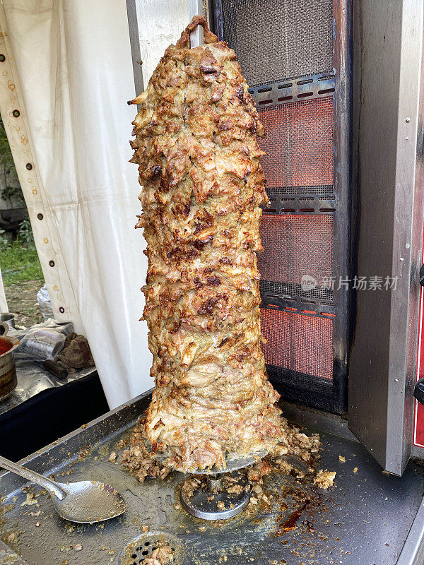 土耳其风格的烤肉串在金属格栅上，肉在垂直旋转的烤炉上烹饪，鸡肉堆叠成倒锥形