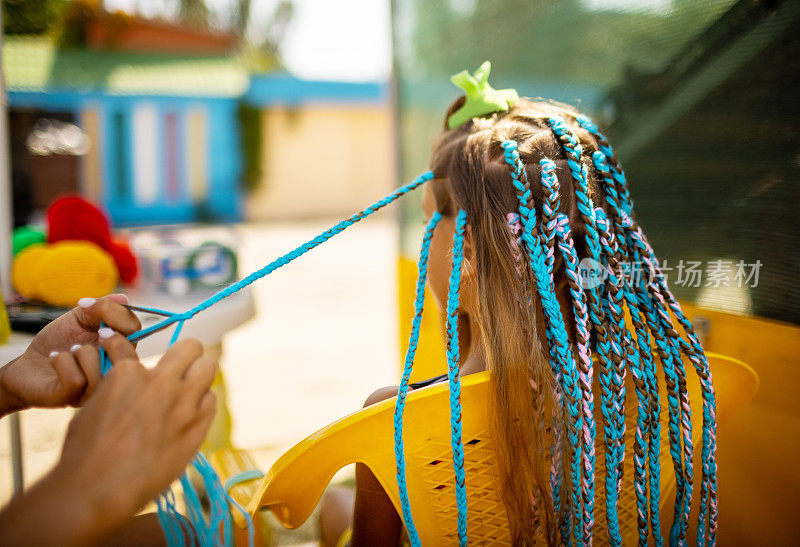 一个穿着西装的女孩在一个阳光明媚的日子里在她的头发上编着非洲辫子